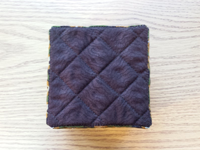 May include: A brown quilted fabric pouch with a green, yellow, and orange patterned border.