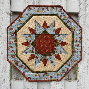 May include: Octagonal table runner with a starburst design in shades of blue, green, brown, and cream. The fabric features a repeating pattern of chickens and other farm animals.
