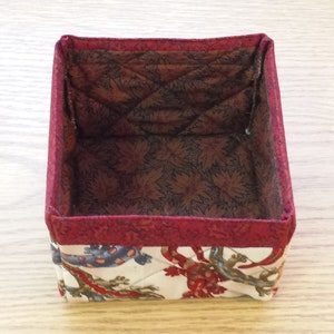 May include: A red and white fabric storage box with a quilted interior. The box is empty and ready to be filled with items.