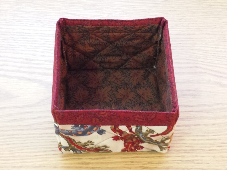 May include: A red and white fabric storage box with a quilted interior. The box is empty and ready to be filled with items.