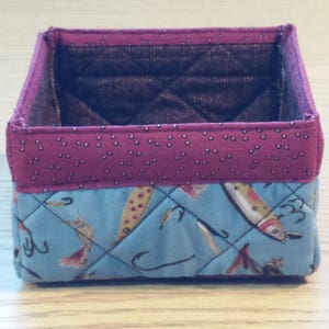May include: A quilted fabric storage box with a red and white polka dot pattern on the top and a blue and white fish pattern on the bottom.