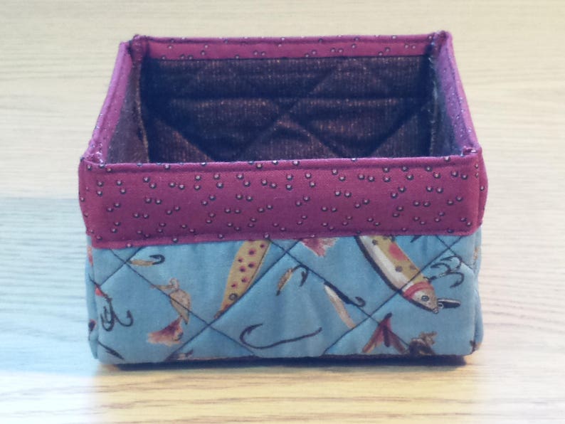 May include: A quilted fabric storage box with a red and white polka dot pattern on the top and a blue and white fish pattern on the bottom.