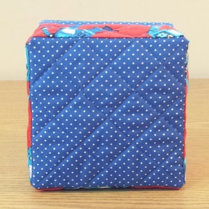May include: A blue and red quilted storage box with white polka dots. The box is made of fabric and has a square shape.