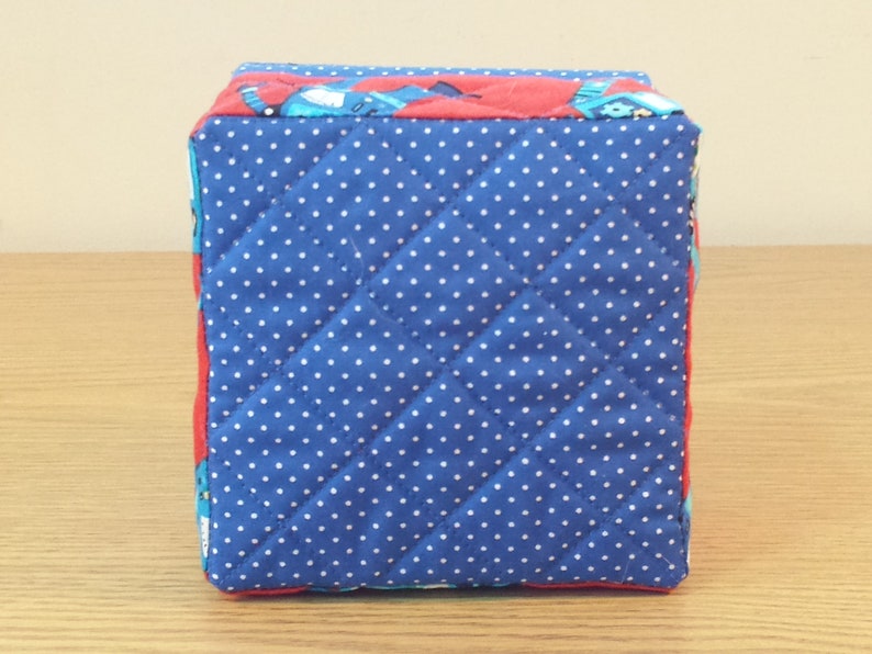 May include: A blue and red quilted storage box with white polka dots. The box is made of fabric and has a square shape.