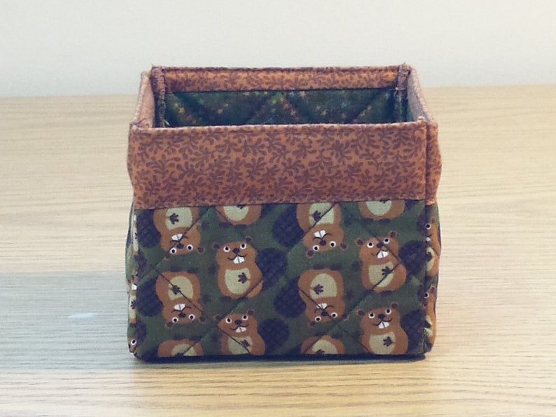 May include: A brown and green fabric storage box with a quilted design. The box is decorated with a pattern of cartoon beavers.