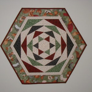 May include: A hexagonal table runner with a geometric design in shades of green, red, and white. The border features a repeating pattern of chickens.