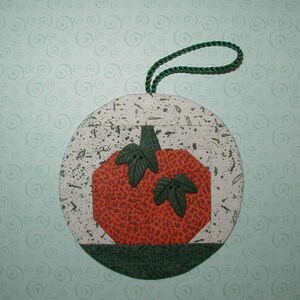May include: A round, green, white, and orange fabric pumpkin ornament with a green stem and leaves. The ornament has a green fabric loop for hanging.
