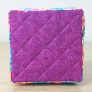 K&ouml;nnte beinhalten: Ein kleiner, quadratischer, gesteppter Aufbewahrungskorb mit einer rosa Stoffauskleidung und einem bunten Blumendruck auf der Au&szlig;enseite.