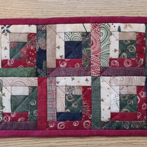 May include: A red, green, and white patchwork quilt square with a log cabin pattern. The quilt square is made of various fabrics with different patterns, including paisley, plaid, and floral.