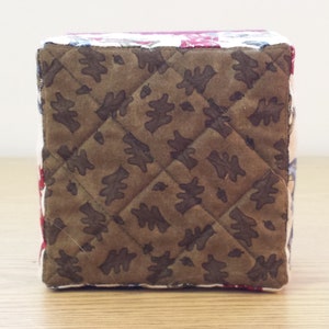 May include: A brown quilted fabric box with a leaf pattern. The box is made of patchwork fabric with different colors and patterns.