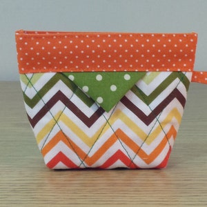 May include: A small orange, green, brown, and white chevron patterned fabric pouch with a zipper closure and a small orange handle.