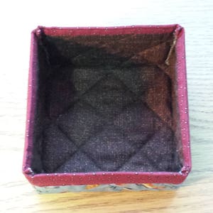 May include: A small, rectangular storage box with a quilted fabric lining. The box is made of a red fabric with white polka dots and has a floral pattern on the bottom.