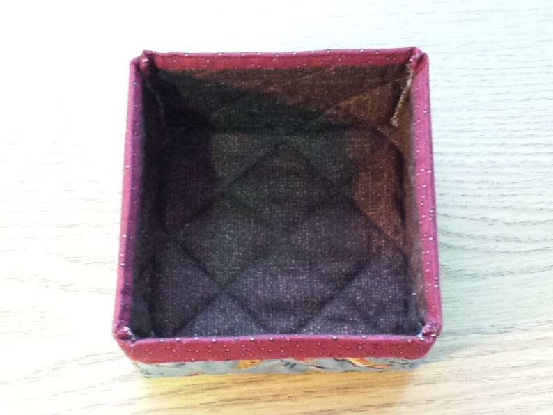 May include: A small, rectangular storage box with a quilted fabric lining. The box is made of a red fabric with white polka dots and has a floral pattern on the bottom.