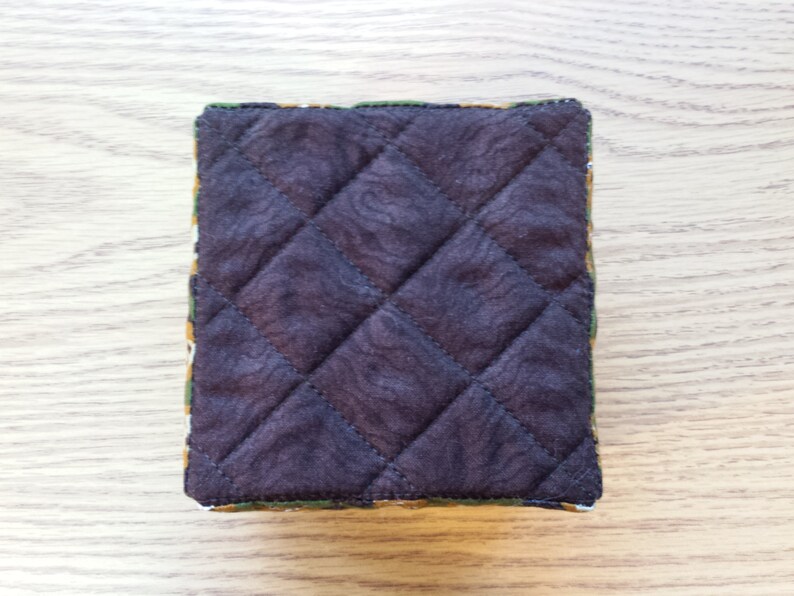 May include: A brown quilted fabric pouch with a green, yellow, and orange patterned border.