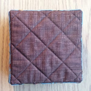 May include: A brown quilted fabric square with a blue trim. The fabric has a subtle diamond pattern.