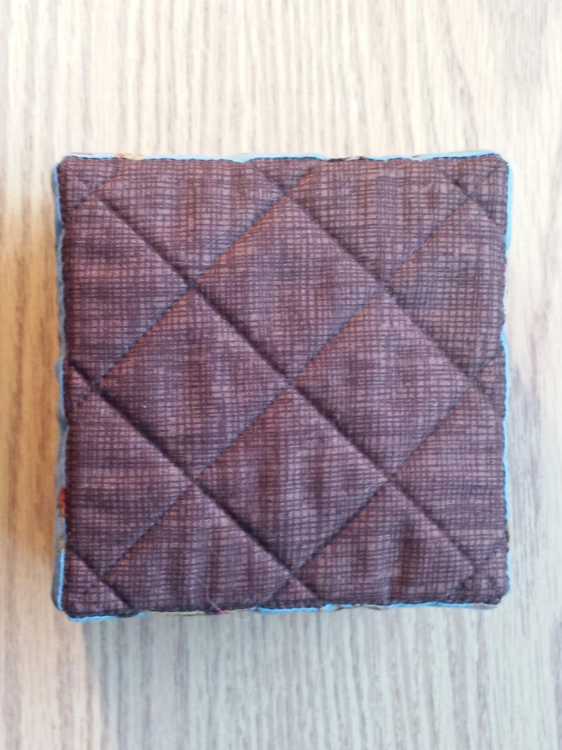 May include: A brown quilted fabric square with a blue trim. The fabric has a subtle diamond pattern.