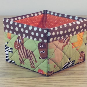 May include: A brown and white polka dot fabric storage bin with a green quilted fabric lining. The lining features a pattern of zebras, giraffes, and other animals.