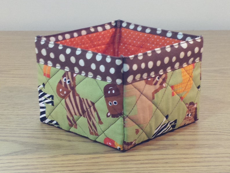May include: A brown and white polka dot fabric storage bin with a green quilted fabric lining. The lining features a pattern of zebras, giraffes, and other animals.