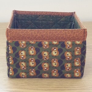 May include: A brown and green fabric storage box with a quilted pattern of cartoon beavers. The box has a brown fabric trim around the top.