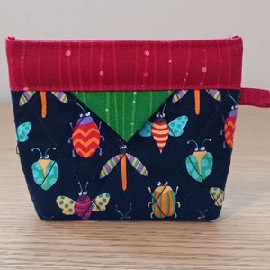 May include: A small, quilted zippered pouch with a red, green, and black fabric design. The fabric features a repeating pattern of colorful bugs and butterflies.