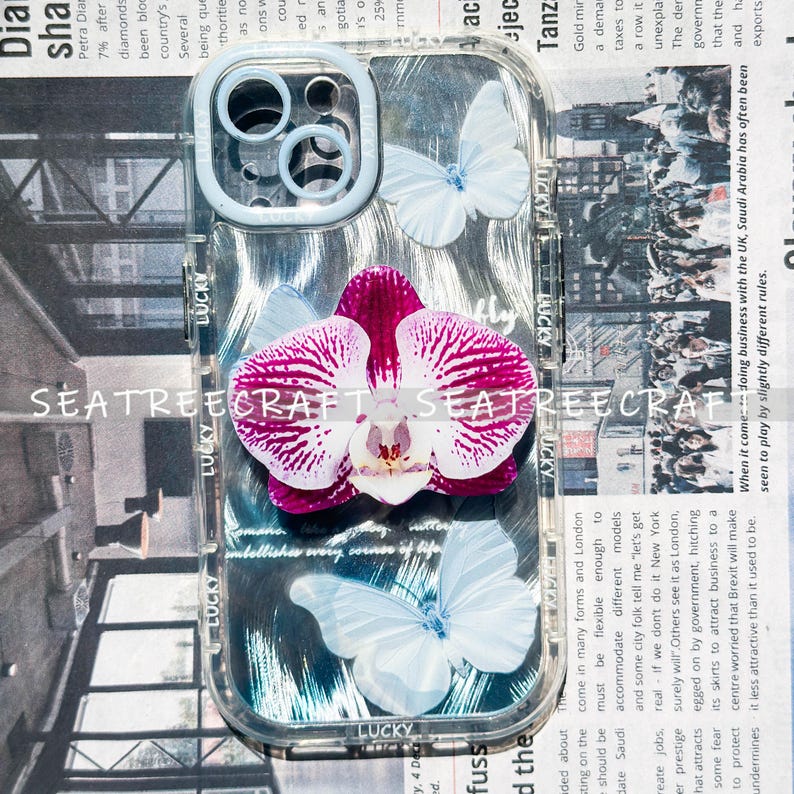 May include: Clear phone case with a purple and white orchid and white butterflies. The case has the word "LUCKY" printed on it. The case is designed to fit a phone.