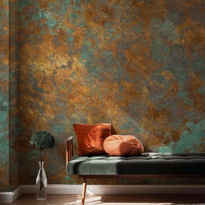 May include: A room interior featuring a textured wall with a blend of copper, teal, and gold tones. A green velvet bench with orange pillows and a knitted pouf sits below the wall. A clear vase with a green plant is on the left.