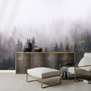 May include: A white armchair with a gold metal frame sits in front of a dark wood cabinet. The cabinet is in front of a wall with a foggy forest scene printed on it. A white ottoman sits in front of the chair.