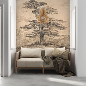 May include: A light beige sofa with a brown blanket and pillows sits in a room with a white wall and a large drawing of a tree on the wall. A woven pendant light hangs above the sofa.