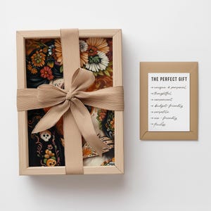 May include: A framed print of a colorful illustration featuring a woman with flowers in her hair. The print is wrapped in brown ribbon and placed in a wooden box. The box is labeled "THE PERFECT GIFT" with a list of reasons why it is a perfect gift.
