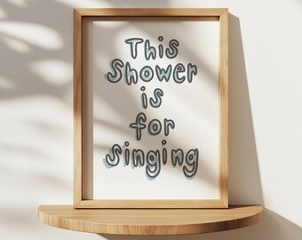 May include: A framed print with the text "This Shower is for Singing" in a light blue and grey font on a white background. The frame is made of light brown wood.