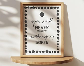 Könnte beinhalten: Ein gerahmter Druck mit dem Text "you will NEVER regret waking up SOBER" in schwarzer Schrift. Der Rahmen ist hellbraun und der Druck hat einen Rand aus schwarzen Punkten. Der Druck wird auf einem Holzregal angezeigt.