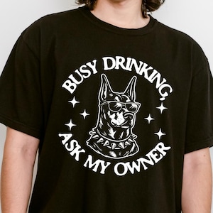 ドーベルマンの飲酒Tシャツ、面白い犬のお父さんへのギフト、忙しい飲酒は飼い主に聞いてくださいTシャツ、ウイスキー好きのシャツ、ドーベルマンの飼い主へのギフト、コンフォートカラーズTシャツ