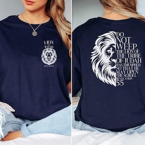 May include: Navy blue t-shirt featuring a white lion graphic with the text "LION OF JUDAH" on the front. The back of the shirt displays a lion graphic and the text "DO NOT WEEP. THE LION OF THE TRIBE OF JUDAH HAS TRIUMPHED... Revelation 5:5."