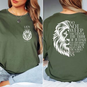 May include: Olive green t-shirt with a white lion graphic and text. The front of the shirt displays a lion's head and the words "Lion of Judah". The back features a larger lion graphic and the text "Do Not Weep. Revelation 5:5".