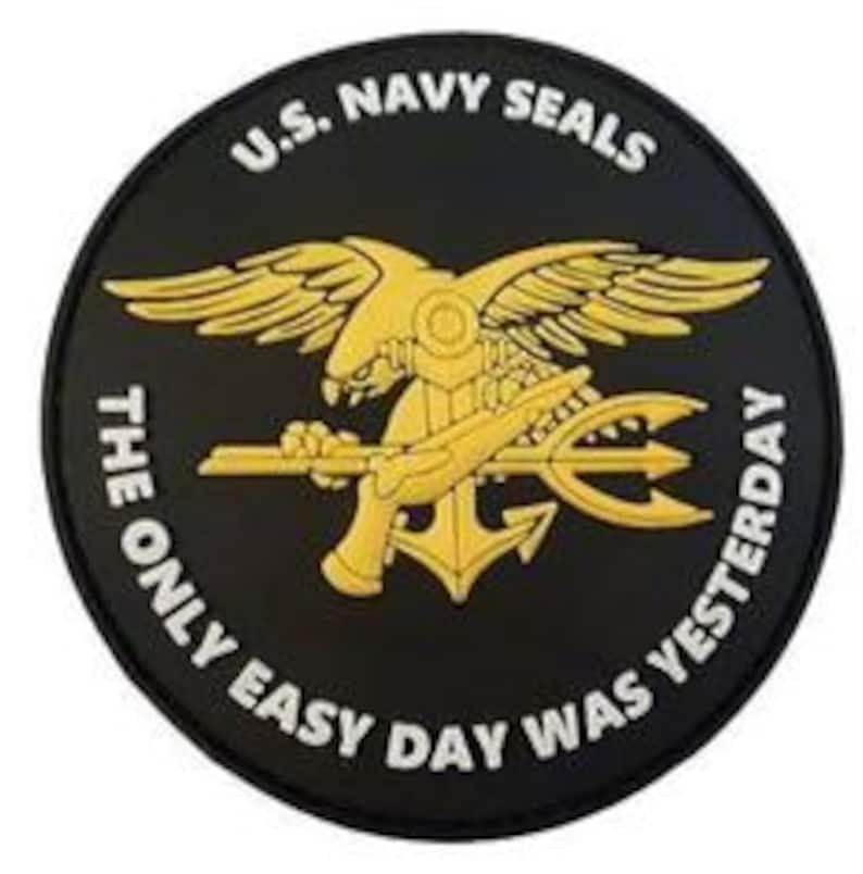 May include: A black and gold round patch with the U.S. Navy Seals logo. The logo features a bald eagle with wings spread, holding a pistol and trident. The text "U.S. NAVY SEALS" is written in white above the logo, and "THE ONLY EASY DAY WAS YESTERDAY" is written in white below the logo.