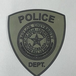 May include: A green and black patch with the words "POLICE" and "DEPT." and the Baylor University seal. The seal features a star and the words "Baylor University", "Pro Ecclesia", "Pro Texana", "Chartered in 1845 by the Republic of Texas".