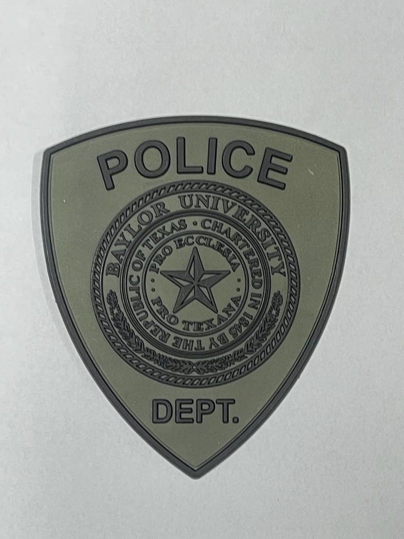May include: A green and black patch with the words "POLICE" and "DEPT." and the Baylor University seal. The seal features a star and the words "Baylor University", "Pro Ecclesia", "Pro Texana", "Chartered in 1845 by the Republic of Texas".
