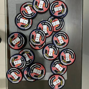 May include: A collection of 18 round black and white patches with red accents. Each patch features a domino with the text "CP AIX-LUYNES" and "&Eacute;QUIPE 1" in French. The patches are arranged in a circular pattern on a glass table.
