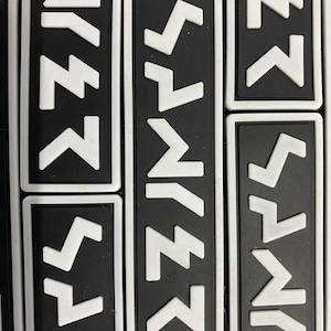May include: A close-up of several black and white patches with a white zig-zag pattern. The patches are rectangular and have a white border.