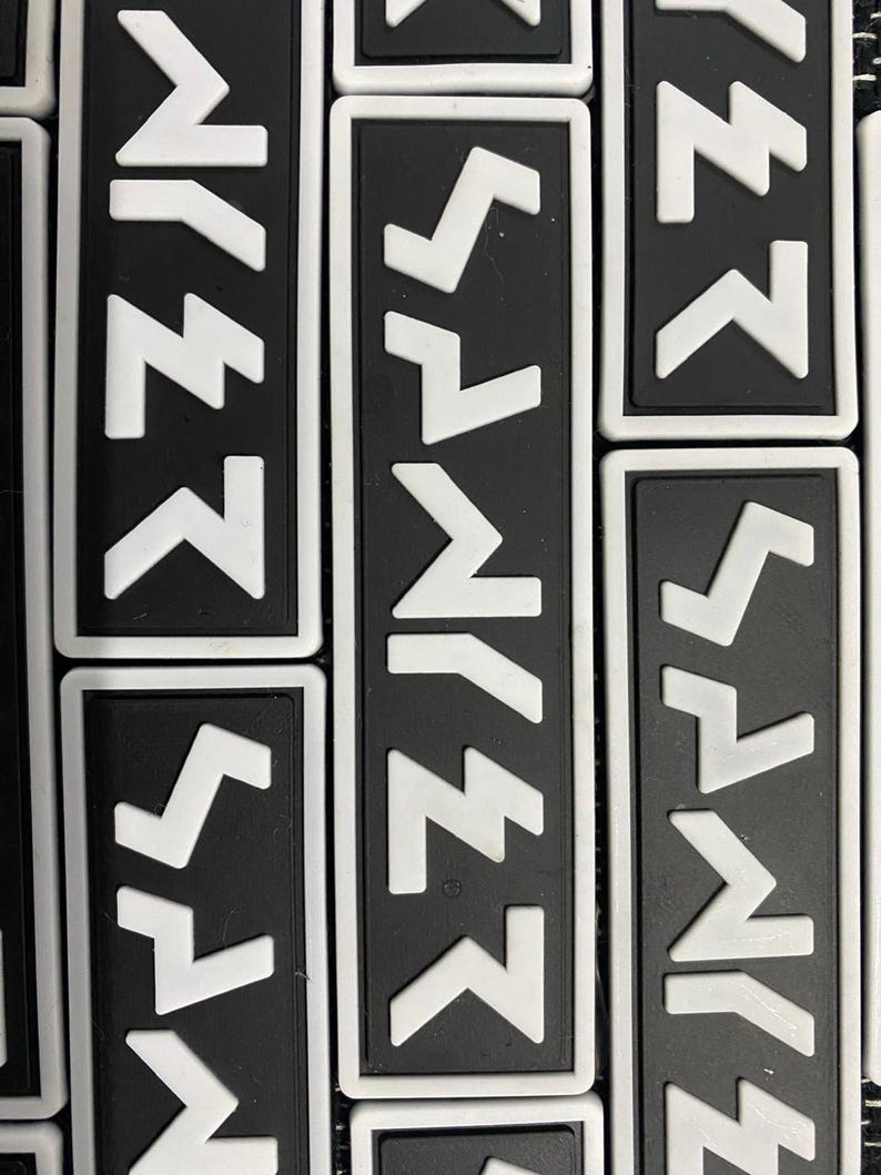 May include: A close-up of several black and white patches with a white zig-zag pattern. The patches are rectangular and have a white border.
