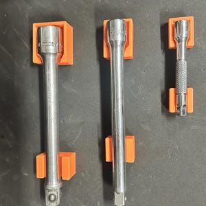 May include: Three metal socket wrenches of varying lengths are held in place by bright orange holders. The wrenches have different sizes, including 1/2 and 3/8 inch markings. The tools are arranged vertically against a dark surface.