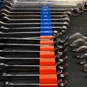 May include: A collection of shiny, silver wrenches of various sizes, neatly arranged. The wrenches are organized with blue and orange size markers. The sizes are labeled in fractions, including 3/8, 7/16, 1/2, 9/16, 5/8, 11/16, 3/4, and 13/16.