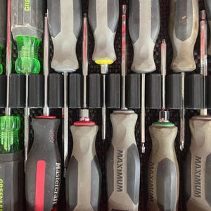 May include: Assortment of screwdrivers with gray and black handles, organized in a red toolbox. Brands include GREENLEE, Mastercraft, and MAXIMUM. The screwdrivers have various colored tips and handle accents, including red, green, and yellow.