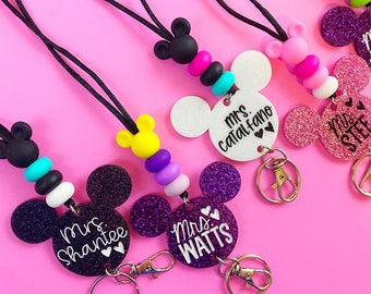 May include: Four colorful lanyards with Mickey Mouse ears and glitter charms. Each charm has a teacher's name, "Mrs. Watts", "Mrs. Shantee", "Mrs. Catalfano", and "Mrs. Stee".