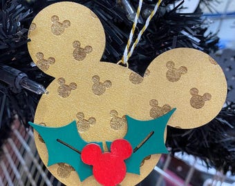 Può includere: Addobbo natalizio Mickey Mouse dorato con una testa di Topolino rossa e foglie di agrifoglio verdi.