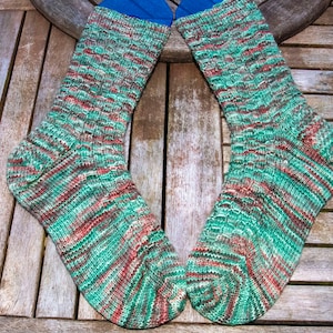May include: A pair of green, red, and white patterned socks with blue cuffs. The socks are laid out on a wooden surface.