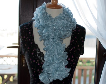 Peut inclure: Une écharpe à volants bleu clair en laine. L'écharpe est drapé sur un mannequin avec une robe à fleurs noires et blanches.