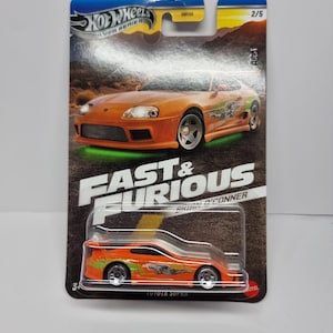 Puede incluir: Coche de juguete Hot Wheels Toyota Supra naranja y verde de la serie Silver de Fast & Furious. El embalaje presenta la imagen del coche y el texto "Fast & Furious" y "Brian O'Conner".