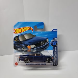 May include: A Hot Wheels die-cast model of a dark blue '89 Mercedes-Benz 560 SEC AMG. The car is displayed on a blue and white card with the Hot Wheels logo and the text "CARROSSERIES LARGES ET FÉROCES".