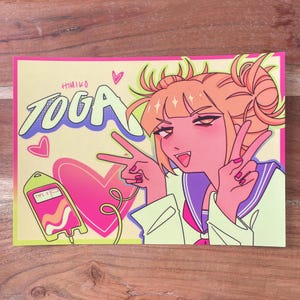 May include: A colorful illustration featuring a character with orange hair in a school uniform, making peace signs. The artwork includes the name "TOGA" in large, stylized letters, a heart, and a blood bag graphic. The background is a light yellow with a pink border.